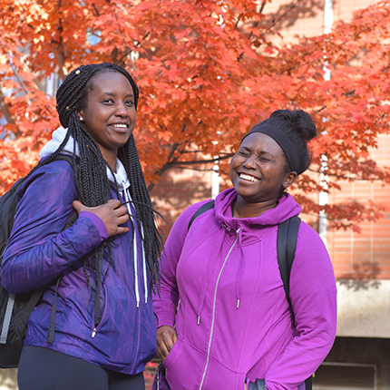 Two students standing infront of a fall tree on campus