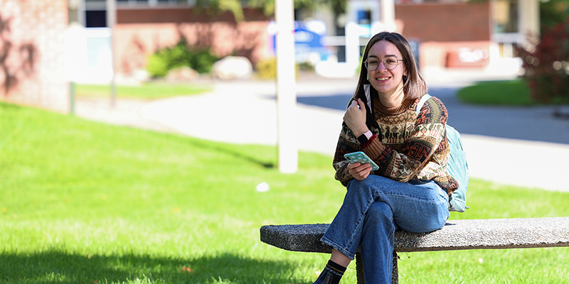 Student seated on campus checking cell phone