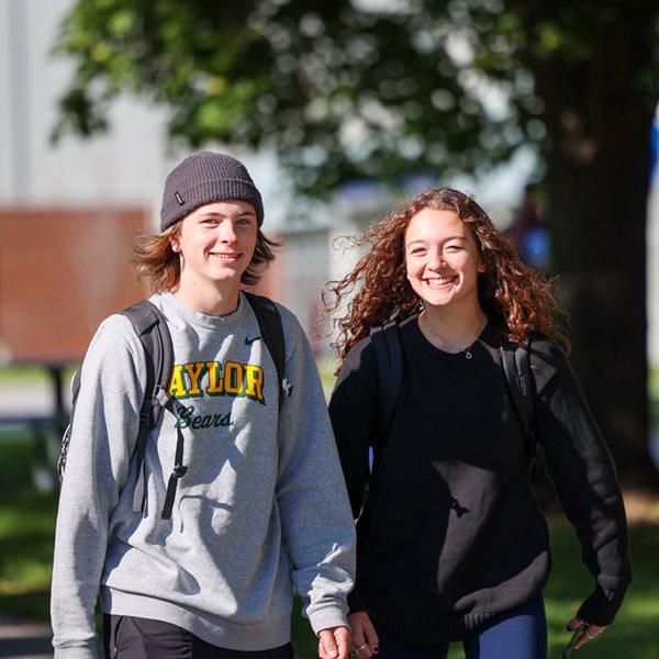 Two smiling students walking to class on campus.